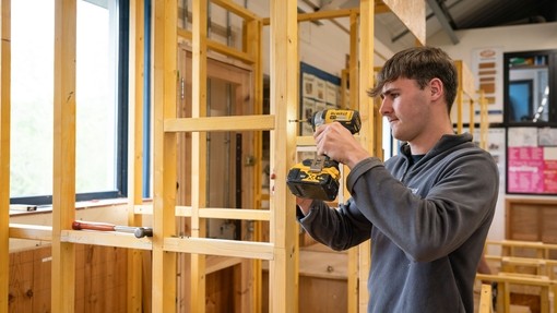 Construction student building a wooden frame with a drill.