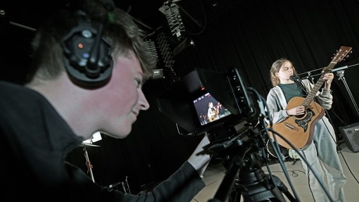 Student in headphones filming someone play the guitar.