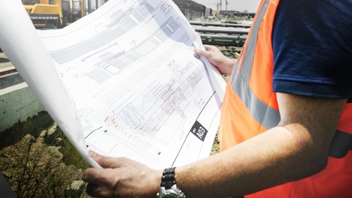 close up of a man in an orange high-vis vest looking at architechtural plans
