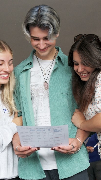 Three students stood close together, looking proudly at the centre student's exam results.