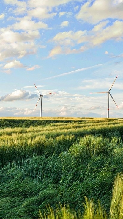 Wind turbines visible in a green field. It's a nice day with clouds in the blue sky