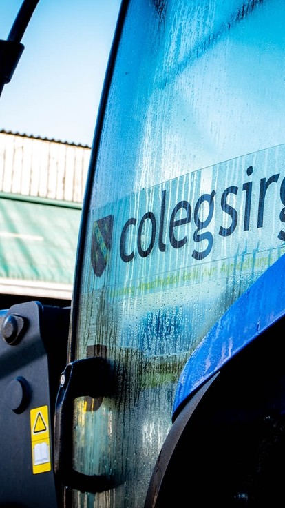 Close-up shot of the side of a blue tractor, the Coleg Sir Gar logo on the side