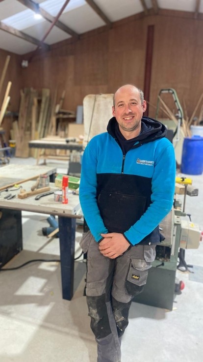 Edward sitting looking at the camera in a carpentry workshop