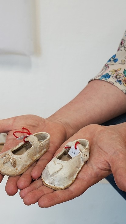 Jenny's hands holding her clay children's shoes with rows of more behind