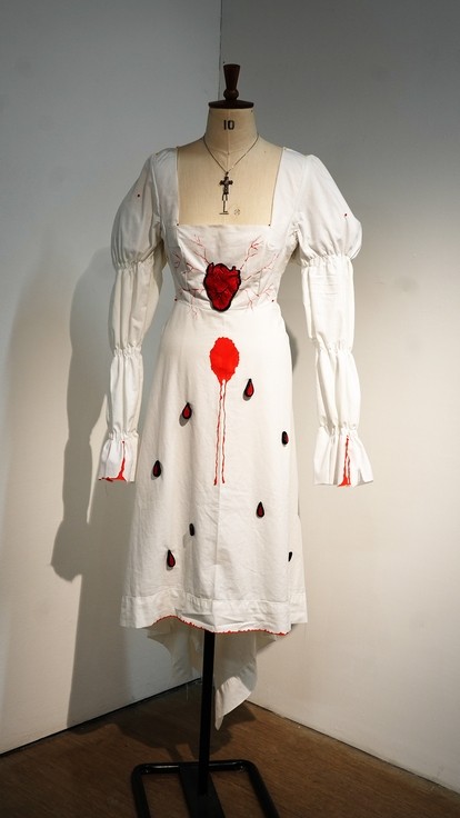A white dress on a mannequin with red hearts that look like blood