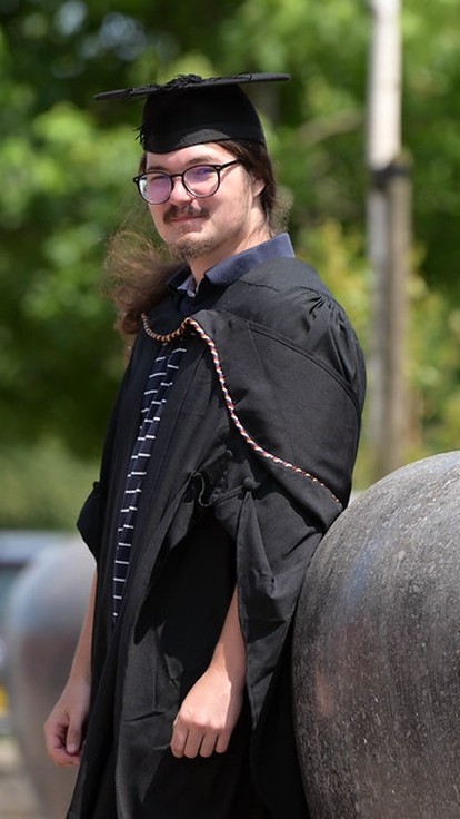 young man with long hair in a graduation cap and gown.
