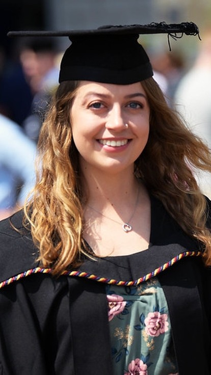 young woman with long hair in a graduation cap and gown.