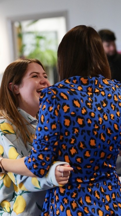 A student hugging her lecturer with people looking happy