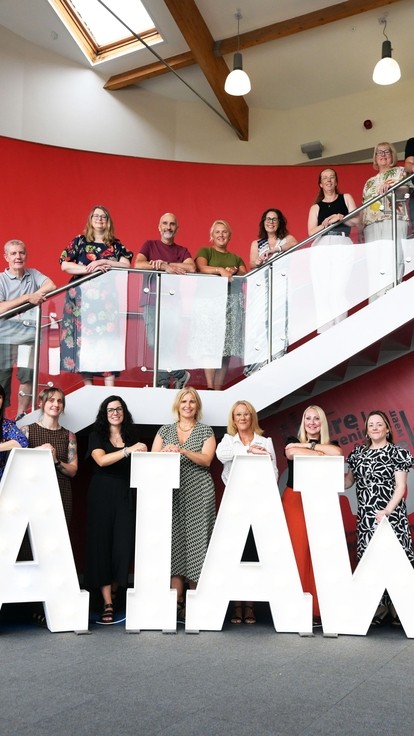 All the A-level tutors lined up on the stairs and balcony with the lighted up words Da Iawn at the bottom 