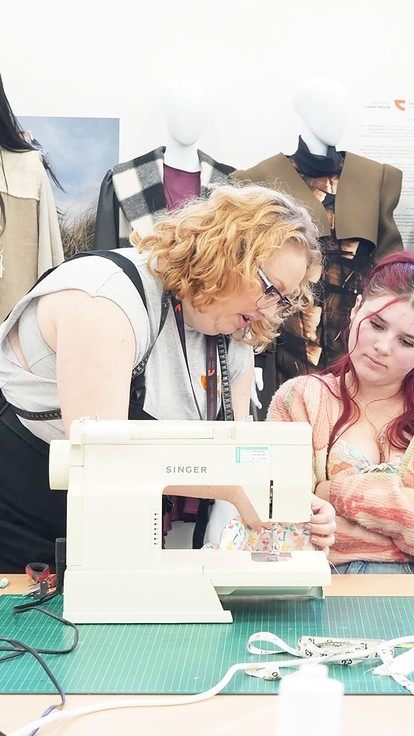 Tammy, resident fashion graduate showing a student what to do on a sewing machine