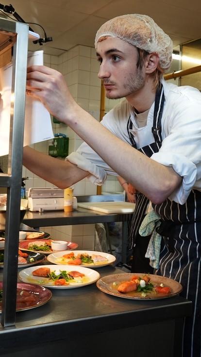 A catering students looking at a sheet of paper at the kitchen pass
