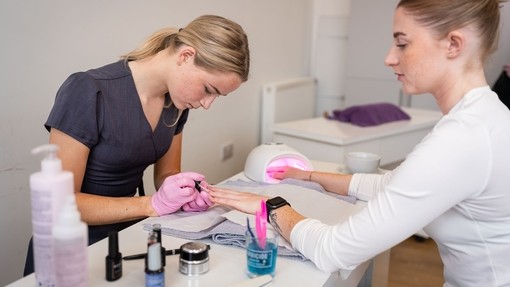 Student in purple uniform giving a client a manicure.