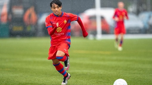 Student in red sports kit playing playing football.