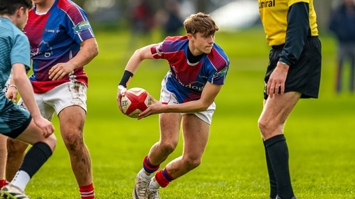 Action shot of student in red and blue sports kit playing rugby.