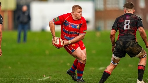 Student in red sports kit about to pass a rugby ball.