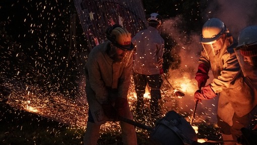 Students in protective clothing working in the metal foundry. The image is dark and highlighted by sparks of metal and fire.