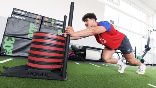 Student in sports kit pushing a sled in the gym.