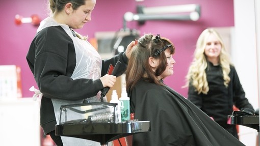Student in black uniform drying a clients hair in a salon.
