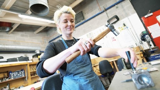 A student with a metal hammer making jewellery.