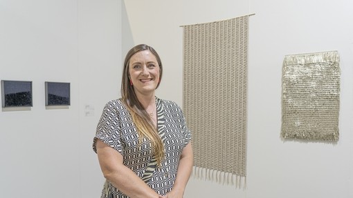 Laura Thomas stood in gallery in front of her artwork