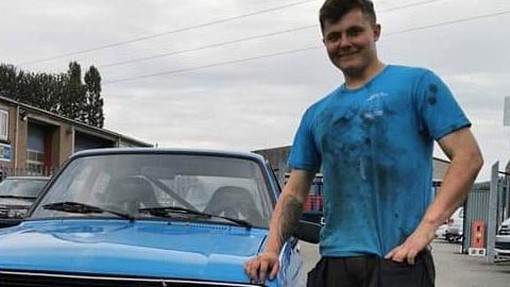 Tom standing in a blue shirt near one car