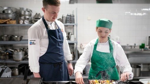 lecturer helping a catering student to grill a kebab