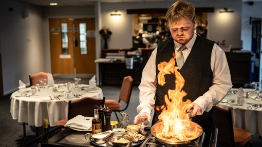 student doing a flambe display in a training restaurant