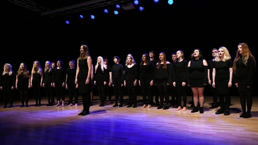 Choir in black singing in a well lit theatre