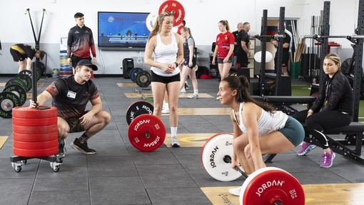 A group of students watching a young woman deadlift