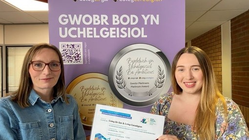 Becky and Ffion from BeAmbitious team holding up award certificate in front of banner