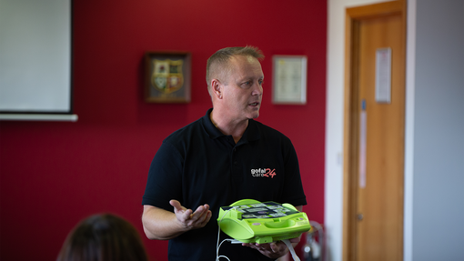 A care24 male tutor teaching a first aid class wearing a black care24 polo shirt
