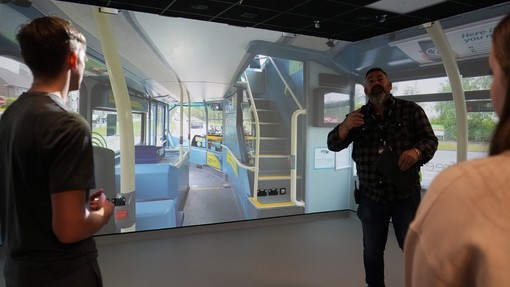 University staff member explaining how the immersive room is used for training. A bus simulator is seen on a digital wall.