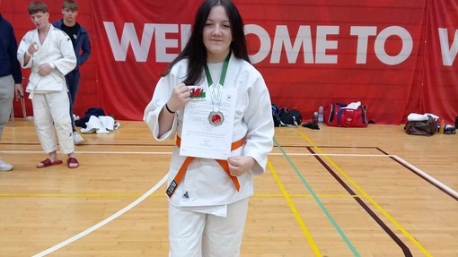 A woman in a white karate uniform proudly holds her certificate, showcasing her achievement in martial arts.