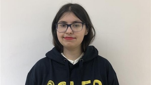 A female student wearing a Coleg Cymraeg hoodie in yellow and grey looking at the camera
