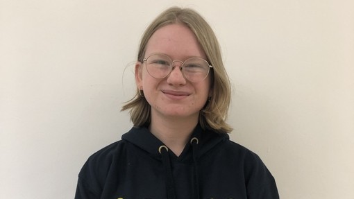 A female student wearing a Coleg Cymraeg hoodie in yellow and grey looking at the camera