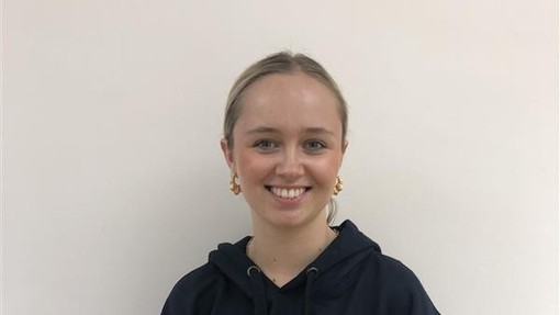 A female student wearing a Coleg Cymraeg hoodie in yellow and grey looking at the camera