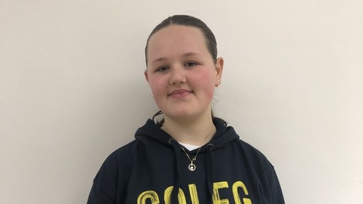 A female student wearing a Coleg Cymraeg hoodie in yellow and grey looking at the camera