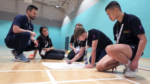 learners sat on the ground in a sports hall completing a mind map during a workshop