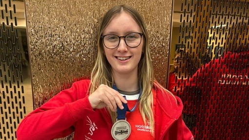 A student dressed in red holding her certificate and silver medal