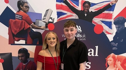 A female student in a red evening dress with a man in black in front of a national winners stand