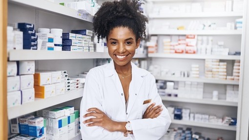 Female pharmacist standing with arms crossed in front of shelves full of medications.
