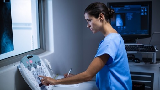 Radiologist in blue scrubs working at a machine with xrays in the background.