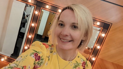 Bryony in a yellow dress (head shot) with mirrors behind with light bulbs around them