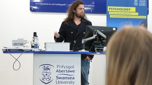 Doctor Kyle talking on a podium with blue Swansea Uni branding