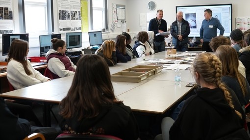 The whole group of students in the class around a table with the society reps at the back with the tutor talking