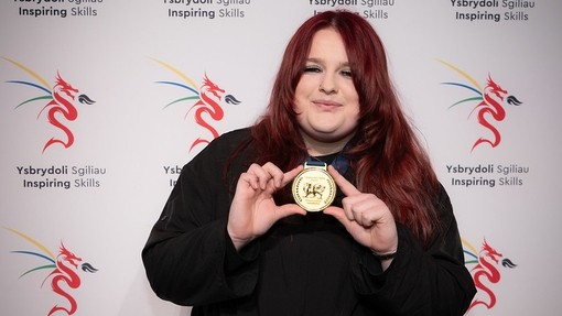 Libby holding her medal with a ISEiW branding behind her