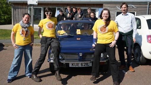 Students surrounding and inside the car with Sister Ally and some are wearing yellow branded Skanda Vale tshirts