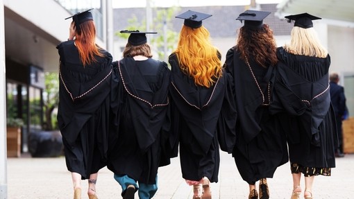 A group of 5 students in graduation caps and gown - they are walking away from the camera in a line