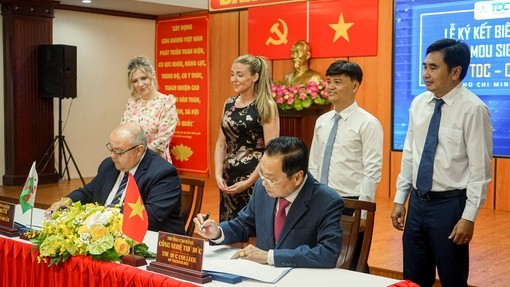 College staff signing the memorandum at a desk with red tablecloth and backdrop with Vietnamese staff