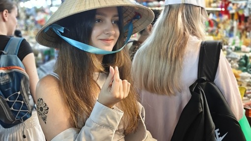 A student in a traditional Vietnamese hat in what looks like an outdoor market